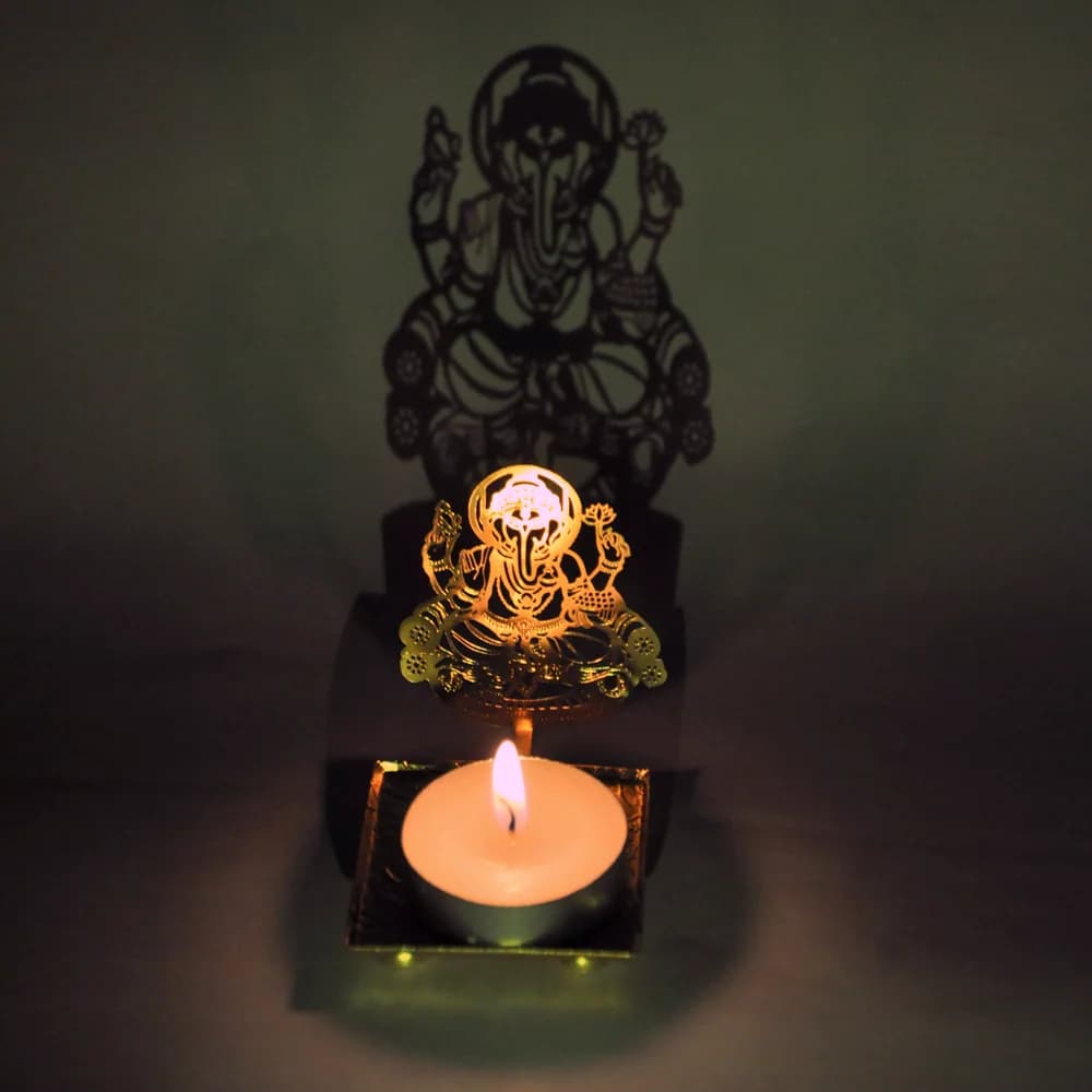 The same diya lit, casting a large Ganesha silhouette on the wall behind it