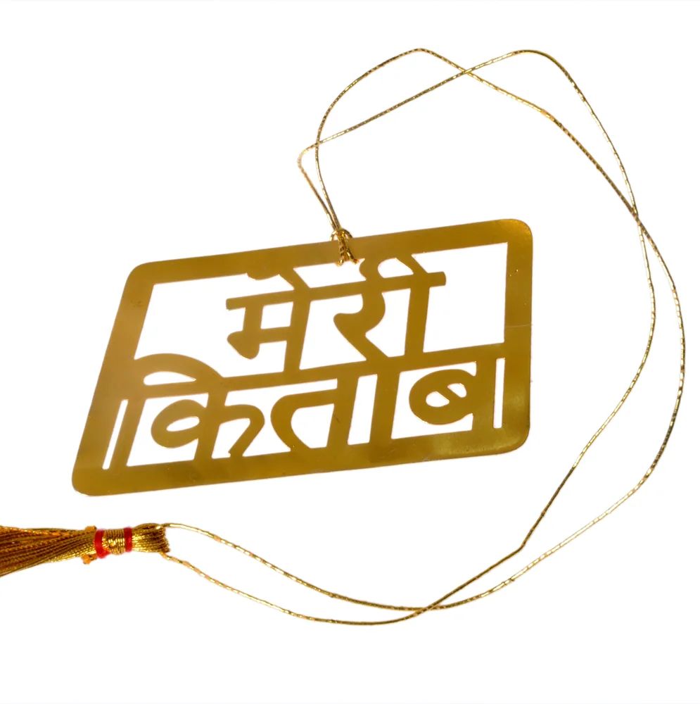 Die-cut gold-tone bookmark reading मेरी किताब in bold Devanagari inside a rectangular frame, on a gold cord with a tassel