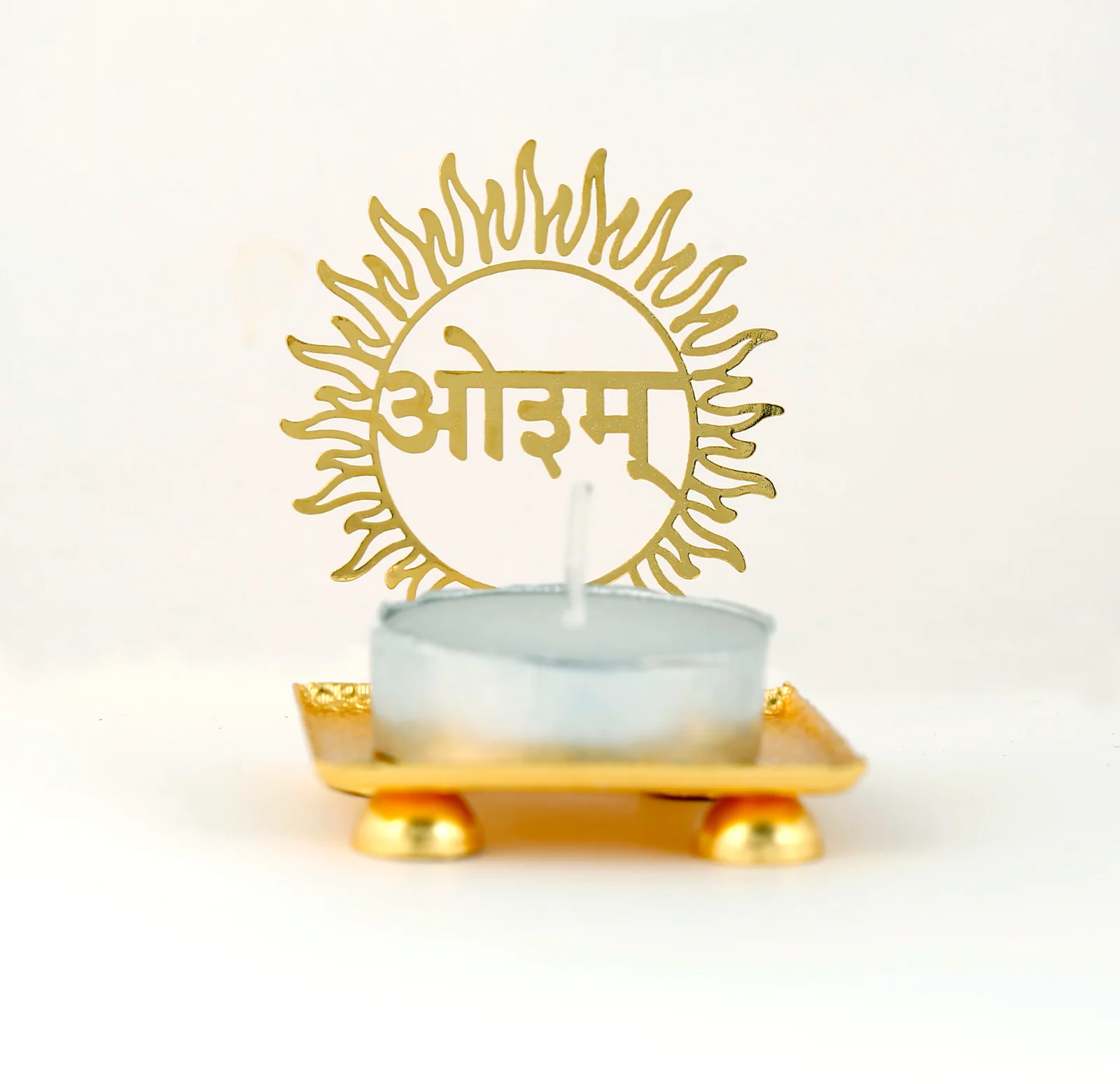 Gold tealight holder cut as an Aum inside a sun disc on a skeletonised leaf, standing on a footed tray, unlit on white