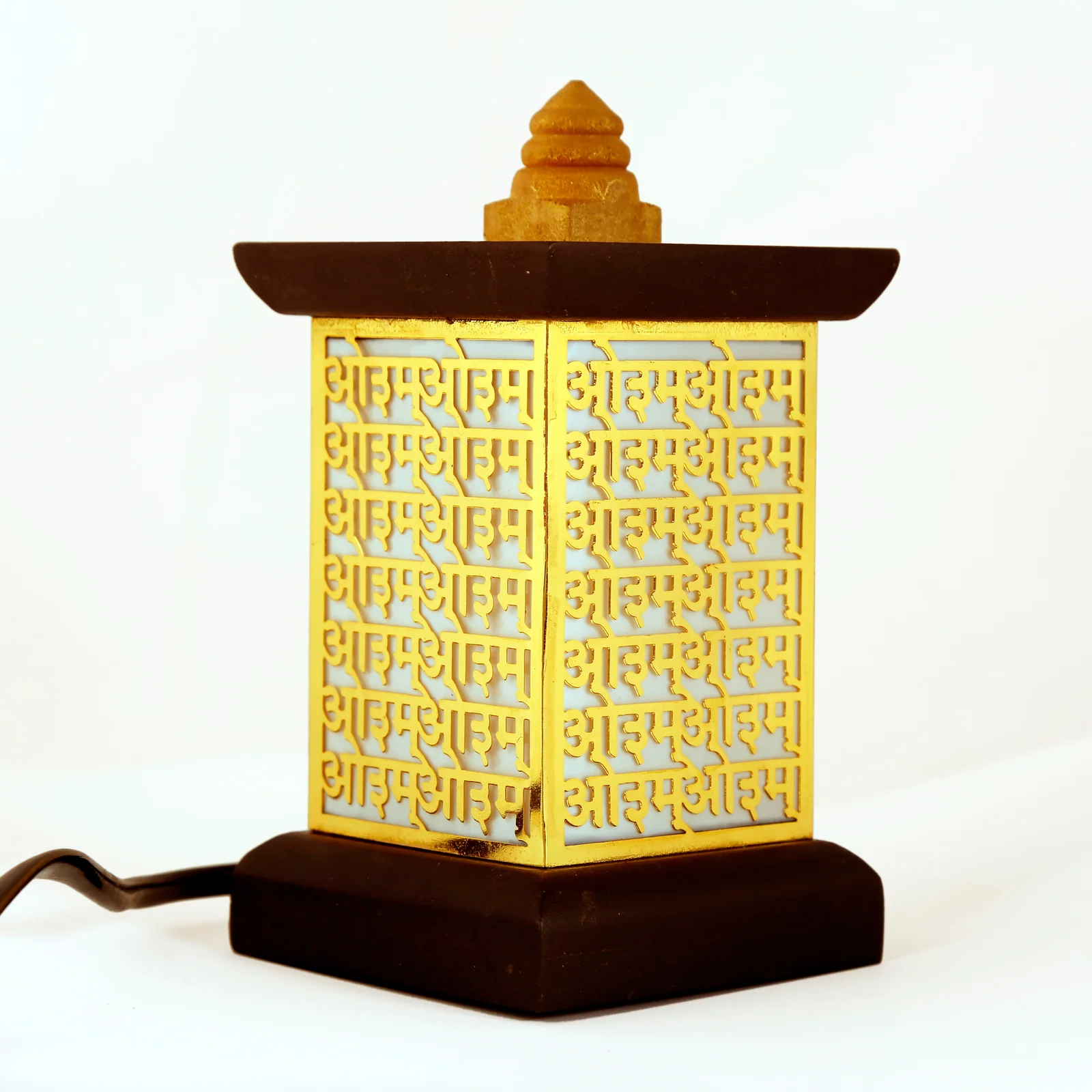 Wooden table lamp with a tall panel of Aum repeated in Devanagari across pierced gold sheet, unlit on white